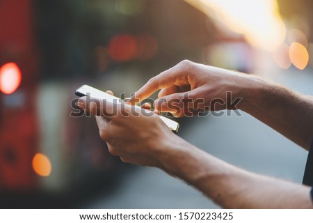 Close-up image of male hands using smartphone at the evening on city at the crossroads, Man typing the messages on social network at the street with sunset on the background