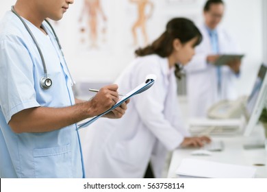 Close-up Image Of Male Nurse Taking Notes In Medical File