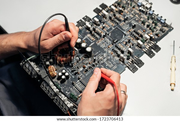 A close-up image of a male technician\'s hand-a\
man measuring the electrical voltage of a car audio amplifier using\
a digital multimeter. Concept of maintenance and repair of computer\
equipment.