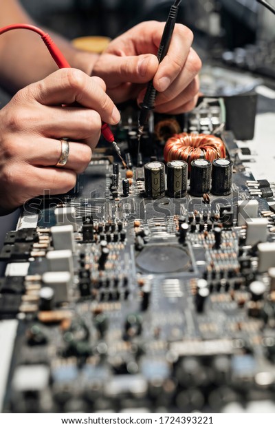 A close-up image of a male technician\'s hand-a\
man measuring the electrical voltage of a car audio amplifier using\
a digital multimeter. Concept of maintenance and repair of computer\
equipment.