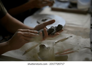 Close-up image of a man in a clay sculpture workshop, molding raw clay to make an ornament at a table in the studio. handcraft, sculptor, craftsman