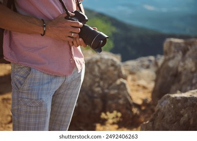 Close-up image of a man holding a camera in an outdoor rocky landscape, emphasizing photography, exploration, and nature.