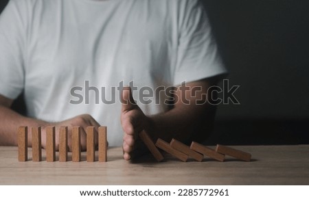 Closeup image of a man try to stop falling wooden dominoes blocks for business solution concept. Risk insurance concept, crisis manager, domino principle