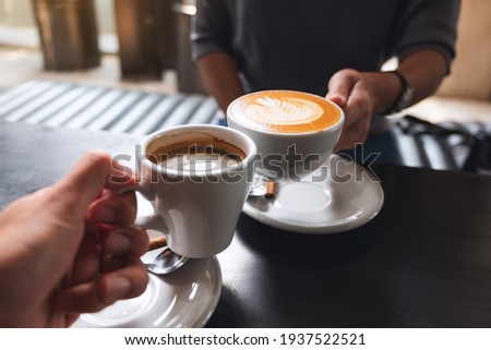 Closeup image of a man and a woman clinking white coffee mugs in cafe