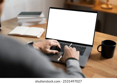 Close-up image of a man working on laptop computer at a table, typing on the laptop keyboard. the laptop with a white screen mockup - Powered by Shutterstock