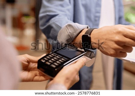 Close-up image of man's hand using smartwatch for contactless payment at a store checkout counter, demonstrating convenience and modern technology in everyday transactions