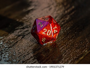 Close-up image of a marbled red 20 sided die on a wet wooden surface outside in the sunlight