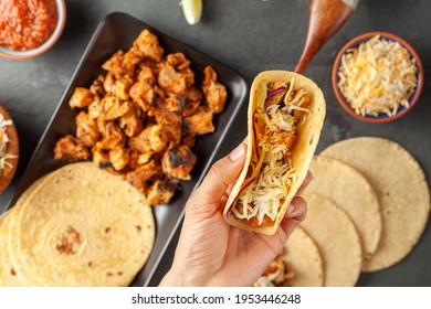 Closeup Image Of A Mexican Taco Dish With Corn Tortillas, Precooked, Preseasoned Chicken Pieces, Cabbage Slaw, Shredded Cheese, Salsa And Cream Sauce And Lime Slices. A Woman Is Holding A Made Wrap.