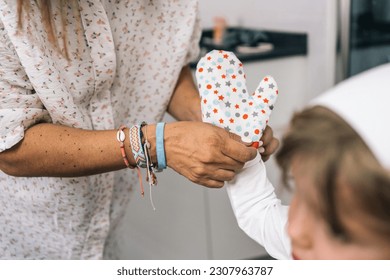 Close-up image of a mother placing an oven mitt on a blond child in a chef's hat.