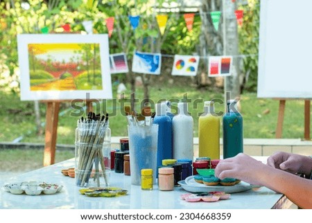Closeup image of painting and coloring equipments, poster color bottles, paintbrushes, and canva paper on table for learing and practising arts, draws and pictures,  soft and selective focus.