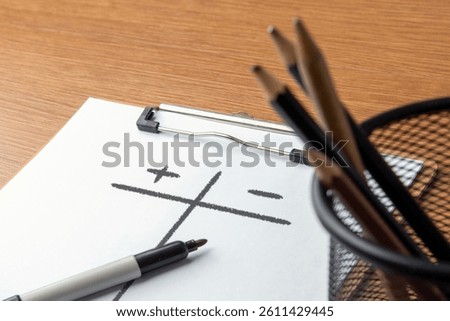 Closeup image of paper clipboard with pros and cons list on wooden table. Assessment, comparison concept.