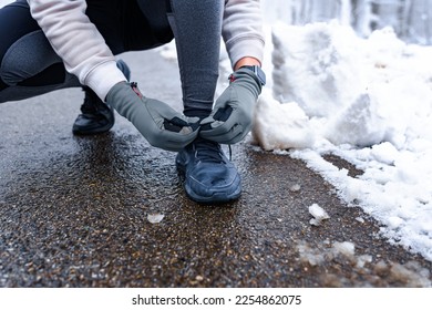 Closeup image of a person tying shoelaces on wet road, snow on the ground and sports equipment in focus. - Shutterstock ID 2254862075