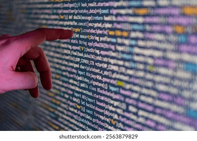 A close-up image of a persons hand pointing at a code display on a large screen, likely in a modern software development workspace or educational setting The hand is wearing a watch