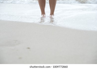 Closeup image of person's legs while standing on the white beach and the sea