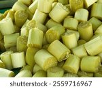 A close-up image of a pile of freshly cut sugarcane pieces. The pieces are arranged closely together, showcasing their light green and yellow colors.