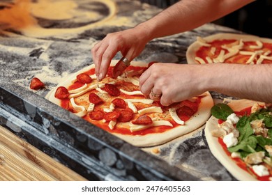 Closeup image of pizzamaker spreading pepperoni on pizza dough - Powered by Shutterstock