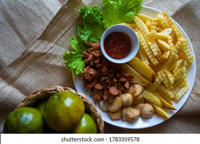 Close-up image a plate of assorted snacks, contains of crinkle-cut fries, wedges potato, meat balls and sausage served with chili sauce.