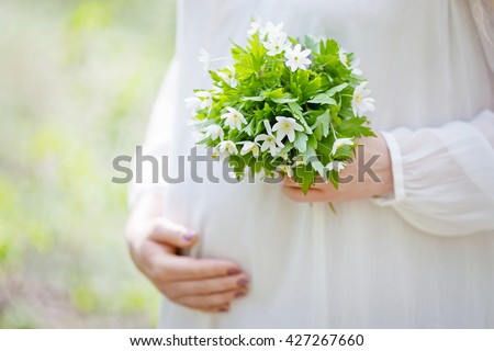 Close-up Image of pregnant woman touching her belly with hands. Focus on a bouquet of white anemones