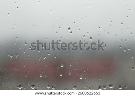 A close-up image of raindrops on a window, with the water droplets visibly clinging to the glass. The background could feature a blurred outdoor scene.
