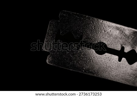 Close-up image of a razor blade on a dark background with the front of the blade in sharp focus down to the back of the blade in detail.