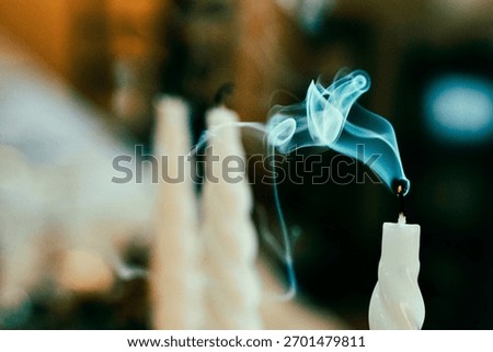 Closeup image of a recently extinguished white candle with smoke gracefully rising from the wick against a blurred background. Captures the ephemeral moment of fading flame serenity.