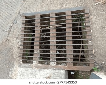 Close-up image of rectangular metal grating embedded in concrete, likely a storm drain or gutter cover