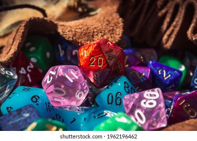 Close-up image of a red marbled 20-sided die on a pile of various colored and shaped dice spilling out of a dice bag in the warm sunlight