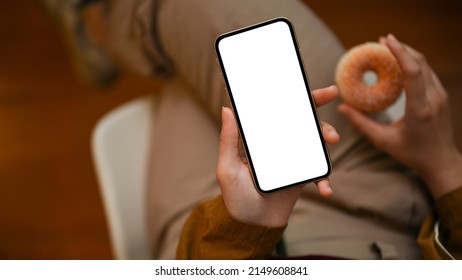 Close-up Image, Relaxed Woman Sitting In The Cafe, Using Smartphone While Eating Donut. Phone White Screen Mockup.