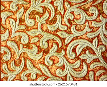 Close-up image of a richly textured wallpaper with an embossed floral and vine pattern. The elegant white and beige swirls stand out against a warm terracotta background, creating a classic.