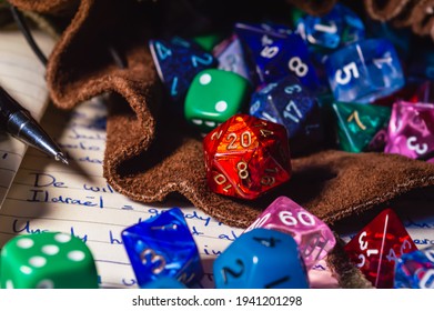 Close-up Image Of Role Playing Dice Of Various Shapes And Colors Spilling Out Of A Leather Dice Bag On A Open Notebook.