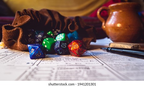 Close-up image of role playing dice of various shapes and colors spilling out of a leather dice bag on a character sheet. With in the background a ceramic drinking jar, a pencil and an eraser