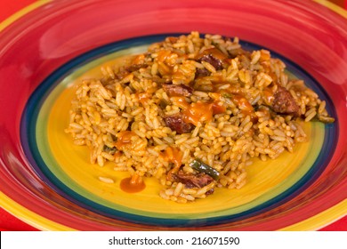 Closeup Image Of Sausage Jambalaya Sprinkled With Louisiana Hot Sauce On Brightly Colored Plate.