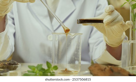 Close-up image of a scientist pouring shampoo samples from a petri dish into a glass beaker. On the table are dried and fresh herbs and soapberry fruits contained in petri dishes. - Powered by Shutterstock