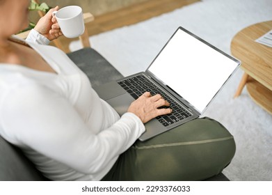 Close-up image of a senior woman sipping coffee while using her laptop on sofa in the living room. laptop white screen mockup - Powered by Shutterstock