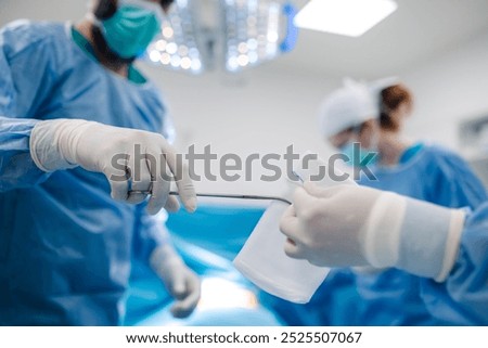 A close-up image showcasing the hands of surgeons passing medical tools back and forth during a surgical operation, highlighting the precision and teamwork in the brightly lit room.