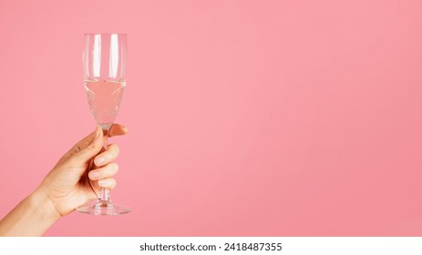 A close-up image showing a hand elegantly holding a sparkling champagne flute with effervescent bubbles, against a soft pink backdrop with ample copy space, cropped, panorama - Powered by Shutterstock