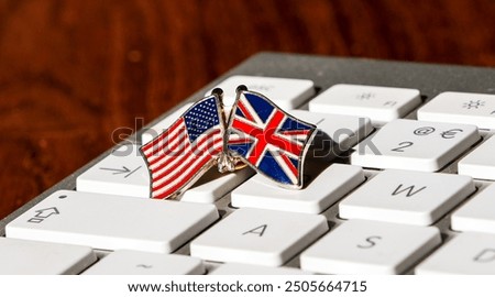 A close-up image of a small pin featuring crossed US and UK flags on a white keyboard, symbolizing international collaboration, digital communication, and the connection between the USA and UK.