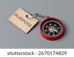 A close-up image of a small, red compass and a wooden keychain tag with the word "PURPOSE". Finding one
