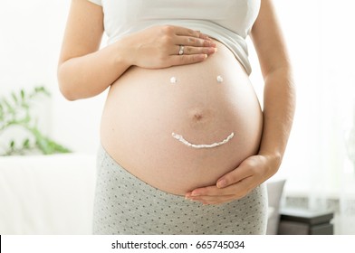 Closeup image of smile sign drawn by creme on pregnant belly