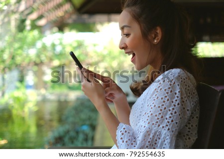 Closeup image of a smiley beautiful Asian woman using and looking at smart phone in outdoor cafe
