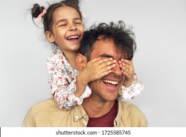 Closeup Image Of Smiling Little Girl Embraces Her Dad, Shares Love Together. Handsome Man Playing With Kid Peekaboo Game. Playful Daughter Cover The Eyes With Hands Of Her Father For A Surprise.