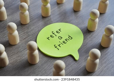 Closeup image of speech bubble with text REFER A FRIEND surrounded by a group of wooden dolls. 