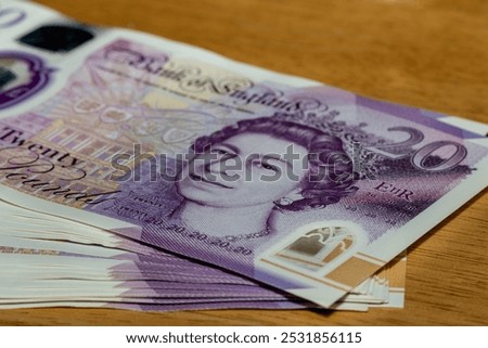 A closeup image of a stack of twenty pound banknotes featuring Queen Elizabeth II on the front, with a wooden surface in the background.