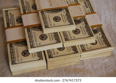 Close-up image of a stack of United States dollar banknotes secured with a paper band, placed over scattered cash. Shallow depth of field highlights financial wealth, savings, and economic concepts.