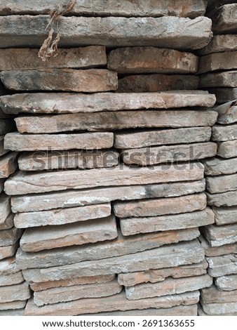 A close-up image of stacked rustic clay bricks, showcasing their rough, weathered texture and eart