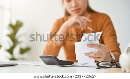 Close-up image of a stressed millennial Asian woman sits at a table, calculating her house installment and planning her monthly expenses.