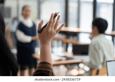 A close-up image of a student raising her hand, asking or answering a question while studying in the classroom. university, high school, education concept - Powered by Shutterstock