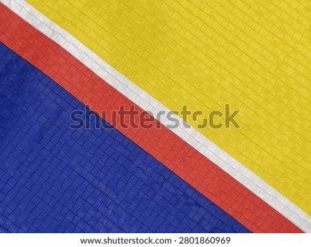 A close-up image of a textured surface featuring three diagonal stripes in yellow, red, and blue separated by thin white lines.
