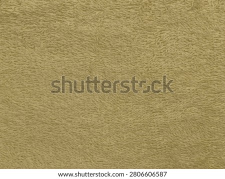 A close-up image of a textured surface resembling a golden or beige fabric, possibly a towel or carpet with soft, looped fibers.
