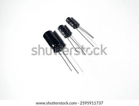 A close-up image of three black electrolytic capacitors with long leads placed on a white background. The capacitors vary in size and voltage ratings, typically used in electronic circuits for energy 